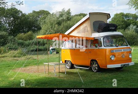 Furgone Classic Orange Volkswagen Camper parcheggiato sul Camp Site dal fiume con rabbocco e tenda Foto Stock