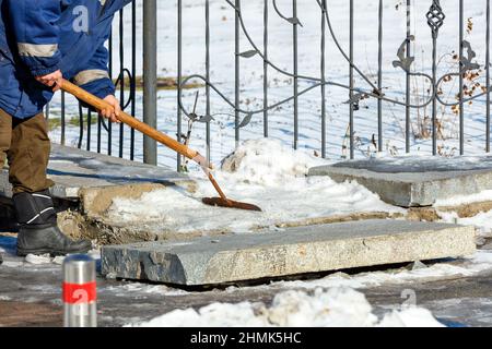 In una giornata invernale limpida, un operatore di servizi pubblici libera la neve e il ghiaccio da un marciapiede di granito su una strada della città. Foto Stock