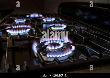 Primo piano di anelli di gas fiammeggiante illuminati sul piano di cottura di un fornello a gas domestico in un ambiente di cucina britannico. Foto Stock