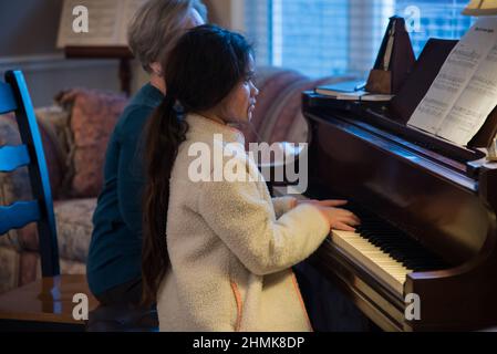 South Jordan, Utah, USA, 10 febbraio 2022. Una bella giovane studentessa di pianoforte si concentra sulla sua lezione. La sua insegnante la guarda ogni mossa. Foto Stock