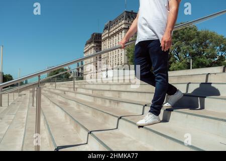 Un latino irriconoscibile con un jean e sneaker bianche che scendono su una scala di cemento. Orientamento orizzontale. Foto Stock