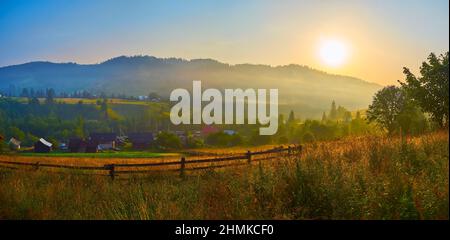 Paesaggio montano panoramico con piccole case in legno, foreste di conifere e prati verdi del villaggio di Dzembronia all'alba, Carpazi, Ucraina Foto Stock