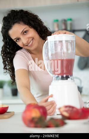 donna con un frullatore moderno che trita frutta e prepara frullati Foto Stock