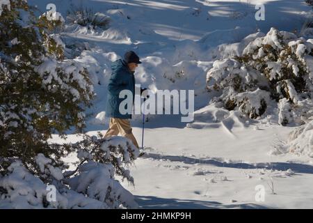 Un uomo anziano cammina lungo un sentiero naturale dopo una tempesta di neve a Santa Fe, New Mexico. Foto Stock