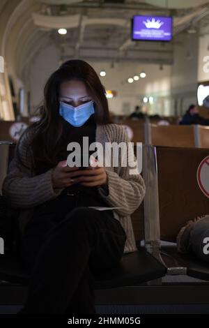 Una giovane donna annoiata è seduta in aeroporto e guardando il suo telefono Foto Stock