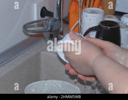 Donna, con solo le mani visibili, lavando piatti Foto Stock