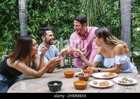 Gruppo di giovani amici latini incontro per birra, bevande michelada e cibo messicano preparare un toast nella terrazza del ristorante in Messico America Latina Foto Stock