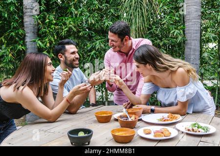 Gruppo di giovani amici latini incontro per birra, bevande michelada e cibo messicano preparare un toast nella terrazza del ristorante in Messico America Latina Foto Stock