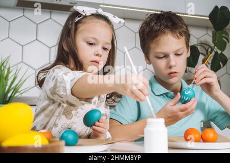 Ritratto di concentrato gioioso due bambini, ragazzo e ragazza, pennello pittura spazzola multicolore uova di galline pasquali su tavola di carta piatto. Rendendo bianco a Foto Stock