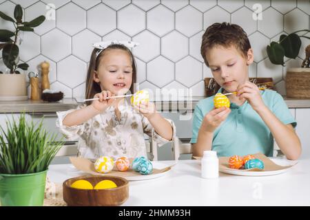 Ritratto di concentrato gioioso due bambini bambini bambini bambina e fratelli ragazzi, pittura multicolore galline di Pasqua uova in cucina su carta tavolo wit Foto Stock