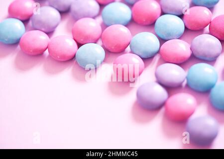 Gli smarties color rosa pastello, blu e viola lavanda creano caramelle su un semplice sfondo rosa chiaro. Primo piano, immagine di banner femminile per Web e social media. Foto Stock
