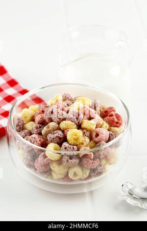 Deliziosi e nutrienti anelli di cereali di frutta aromatizzati in una ciotola di vetro su sfondo bianco Foto Stock