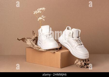 Scarpe ecologiche in pelle. Un paio di sneaker beige con fiori secchi su sfondo marrone. Stile di vita sportivo informale. Foto Stock