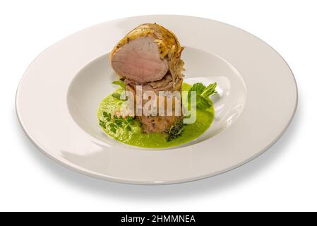 Filetto di maiale al forno su panna di piselli ed erbe aromatiche in piatto bianco isolato su bianco Foto Stock