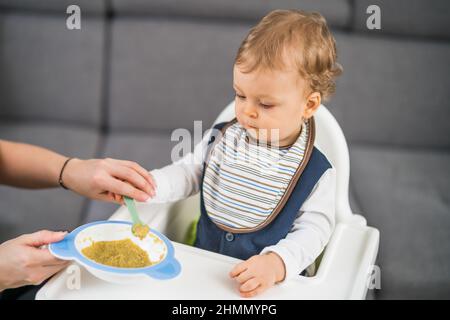 Bambino ragazzo carino imparando a mangiare da solo mentre si siede in un seggiolone. Foto Stock