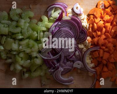 Sedano tritato, cipolla viola, aglio e carote su un asse di legno. Foto Stock