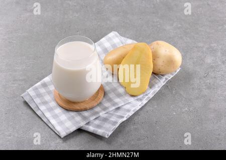 Latte di patate vegano in un bicchiere e tuberi di patate su sfondo grigio tavola di pietra. Primo piano. Prodotto di sostituzione del latte alternativo a base vegetale e privo di lattosio, Trend Foto Stock