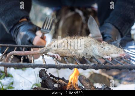 L'uomo senza tetto con coltello a forchetta accanto alla griglia di un ratto, in un paesaggio nevoso, vista ravvicinata. Foto Stock