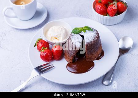 Torta di lava - torta al cioccolato fondente con gelato alla vaniglia, fragole, menta e caffè. Dolci francesi tradizionali. Primo piano. Foto Stock