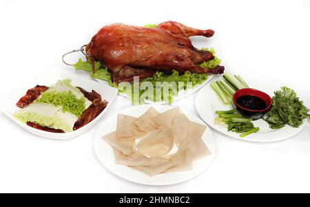 Anatra di Pechino, anatra croccante fritta cinese, servita con salsa di hoisin, frittelle e verdure verdi su sfondo bianco. Foto Stock