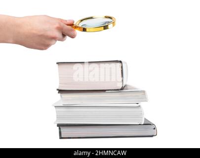 Mano che tiene la lente di ingrandimento sopra i libri impilano isolato su sfondo bianco. Ricerca e studio dettagliato del concetto di informazione. Foto di alta qualità Foto Stock