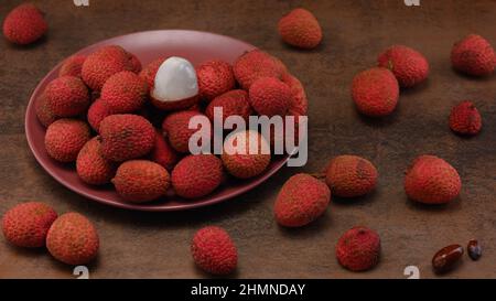 La foto mostra frutti rossi tropicali - lychee. Piatti esotici sullo sfondo color caffè. La foto è fatta in alta qualità. Foto Stock