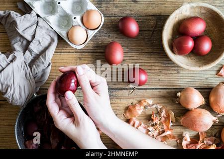 Donna che fa tinto uova di Pasqua dipinte con cipolla colorante naturale su sfondo di legno. Processo di tintura delle uova con vernici naturali per Pasqua. ecol naturale Foto Stock