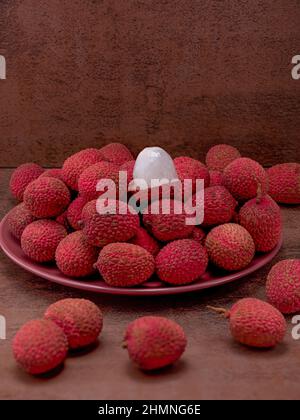 La foto mostra frutti rossi tropicali - lychee. Piatti esotici sullo sfondo color caffè. La foto è fatta in alta qualità. Foto Stock