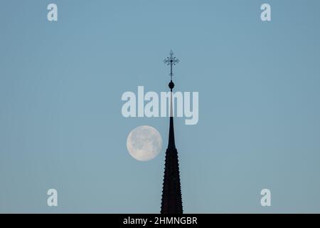 Schaan, Liechtenstein, 19 gennaio 2022 Santa Croce di una chiesa cattolica con la luna piena sullo sfondo al mattino presto Foto Stock