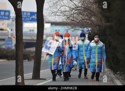 Pechino, Cina. 11th Feb 2022. I volontari che indossano maschere per i Giochi Olimpici invernali del 24th camminano vicino al Nido degli Uccelli a Pechino dopo aver completato il loro lavoro insigns.A CCTV News programma incentrato sui volontari delle Olimpiadi invernali di Pechino. Secondo il suo rapporto, più di 18.000 volontari hanno servito in luoghi diversi all'interno e all'esterno dei Giochi, diffondendo amicizia e calore in modi diversi. Credit: SOPA Images Limited/Alamy Live News Foto Stock