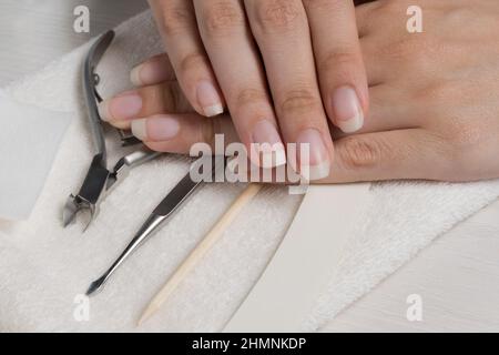 Mani da donna su un asciugamano. Manicure. Attrezzi di manicure, chiodo lucidato. Cura del chiodo domestico, SPA, bellezza. Unghie naturali lunghe. Salone di bellezza. Foto Stock