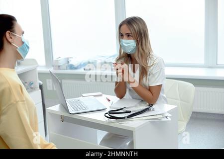 Medico femminile in maschera medica viso hanno consultazione con il paziente durante le pandemie covid-19. Donna in facemask parlare consultare il cliente in clinica o hos Foto Stock
