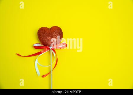 Cuore rosso con nastro bianco e rosso. Simbolo d'amore, fatto a mano su sfondo giallo. Elemento decorativo per San Valentino design, inviti, insenatura Foto Stock