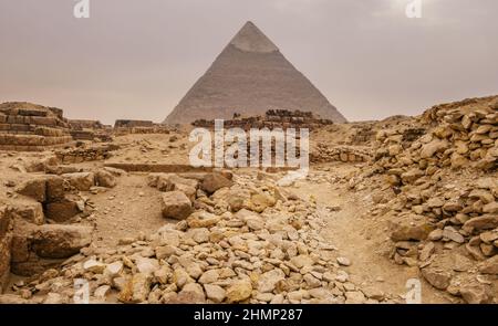 Scavi e rovine nel deserto sullo sfondo di piramide e tempesta di sabbia imminente. Giza, Egitto Foto Stock