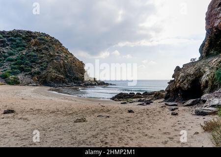 Spiaggia di sabbia appartata su una costa montuosa selvaggia con rocce Foto Stock