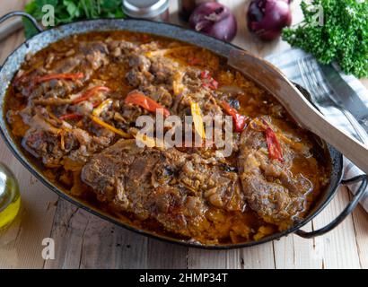 Carne con verdure e salsa. Collo di maiale piccante con cipolle, aglio e peperoni brasati in una padella e serviti su un rustico tavolo di legno. Foto Stock