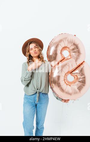 La giovane donna che tiene il pallone mentre si alza su sfondo bianco dello studio celebra la Giornata Internazionale delle Donne Foto Stock