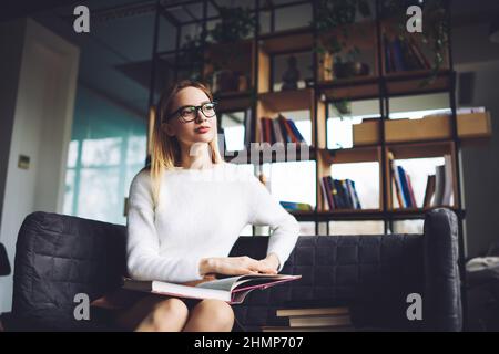 Donna pensierosa seduta in biblioteca con libri Foto Stock