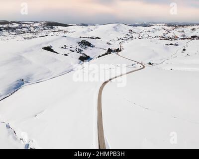 Vista aerea con droni del paesaggio innevato al tramonto. Tortuosa strada asfaltata in montagna. Zlatibor, località di montagna, Serbia, Europa Foto Stock