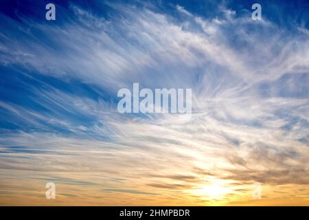 Un cielo drammatico alla fine di una giornata di inverni, il blu striato con alte nuvole di cirro mentre il sole trasforma le nuvole inferiori arancione. Foto Stock