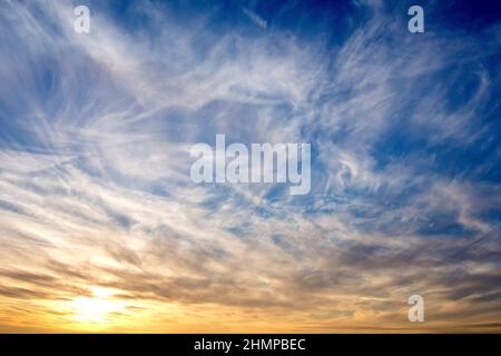 Un cielo drammatico alla fine di una giornata di inverni, il blu striato con alte nuvole di cirro mentre il sole trasforma le nuvole inferiori arancione. Foto Stock