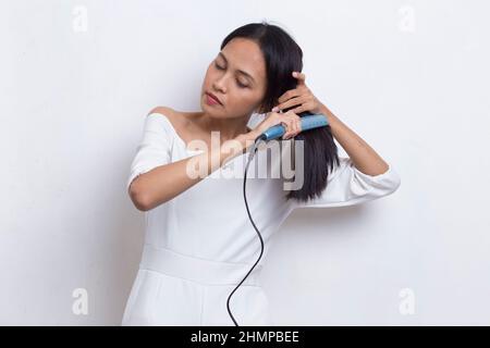 giovane asiatico bella donna felice capelli raddrizzando con capelli piastra su sfondo bianco Foto Stock