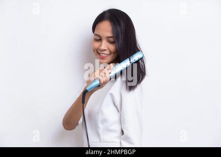 giovane asiatico bella donna felice capelli raddrizzando con capelli piastra su sfondo bianco Foto Stock