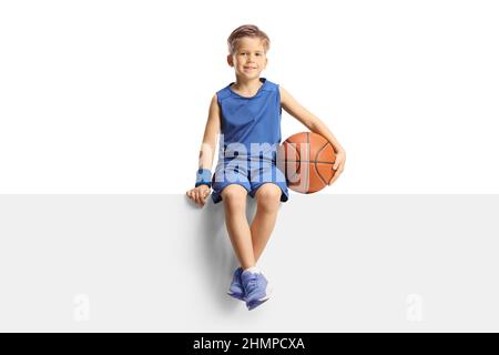 Ragazzo sorridente in una maglia che tiene un basket e si siede su un pannello vuoto isolato su sfondo bianco Foto Stock