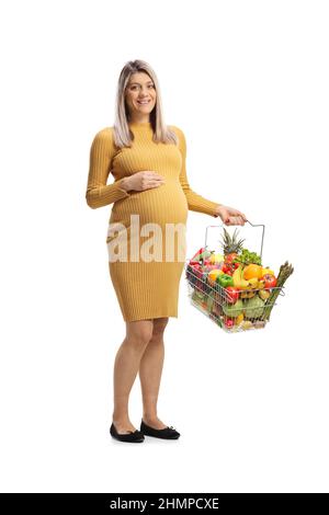 Donna incinta che tiene un cestino di shopping con frutta e verdure isolate su sfondo bianco Foto Stock