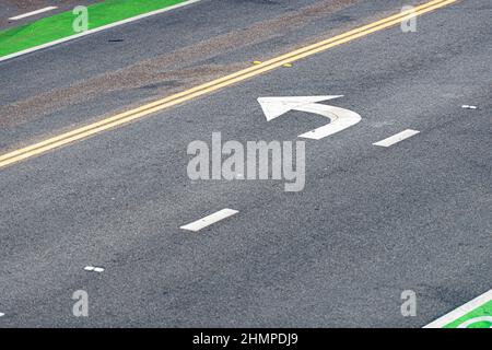 Vista dettagliata asfalto di strada in primo piano. Linea gialla e bianca su nero con freccia indicatore di direzione Foto Stock