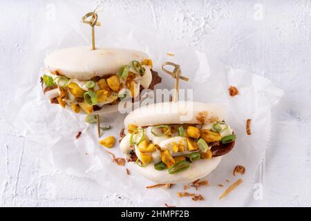 Batè bao bianco vegano fusion asiatico con carne alternativa, mayo e crunchy piccante arachidi Foto Stock