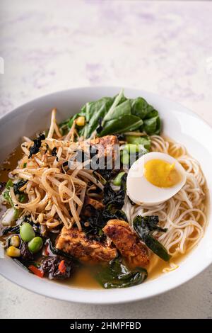 Spaghetti di ramen senza carne di vegano a fusione asiatica con funghi, tofu fermentato, germogli, fagioli, uova di vegan e foglie verdi di pak choi Foto Stock