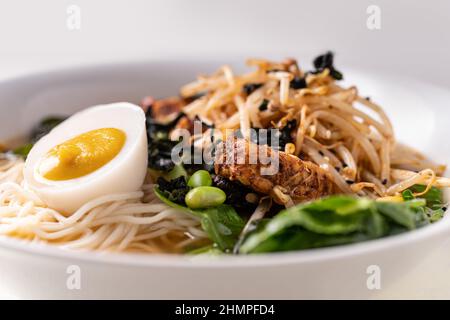 Spaghetti di ramen senza carne di vegano a fusione asiatica con funghi, tofu fermentato, germogli, fagioli, uova di vegan e foglie verdi di pak choi Foto Stock