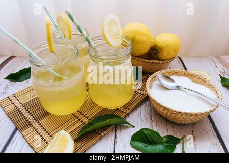 Tre bicchieri di limonata fatta in casa su un tavolo con limoni freschi e una ciotola di zucchero Foto Stock